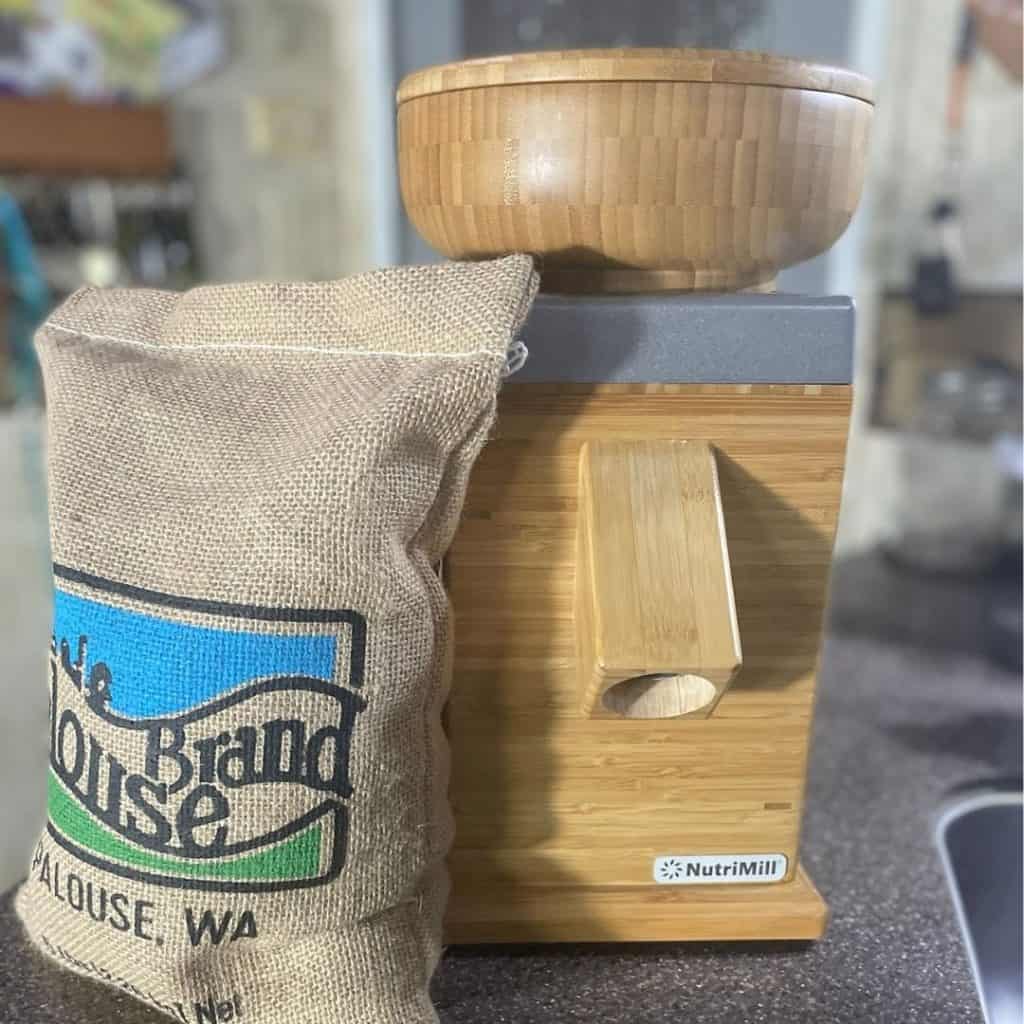 a bag of wheat berries next to a grain mil used to grind flour